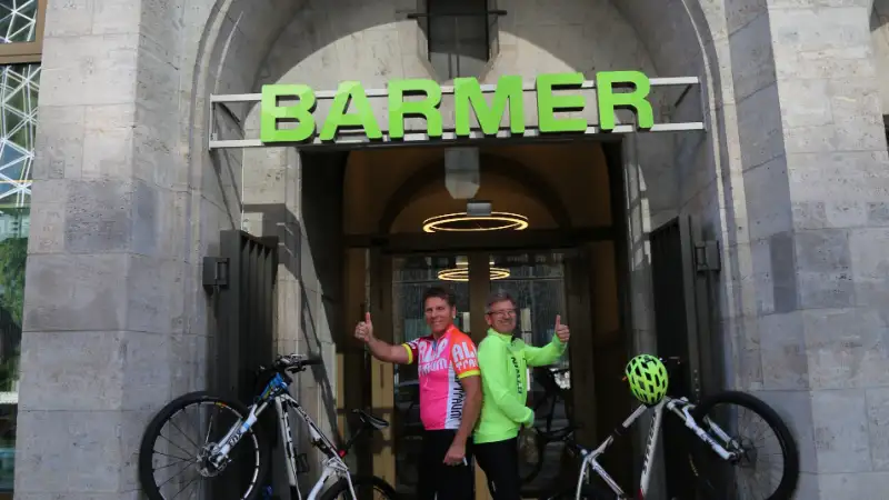 Zwei Barmer Mitarbeiter, die mit ihren Fahrräder ein V in der Eingangspforte von Barmer bilden Zwei Barmer Mitarbeiter, die mit ihren Fahrräder ein V in der Eingangspforte von Barmer bilden