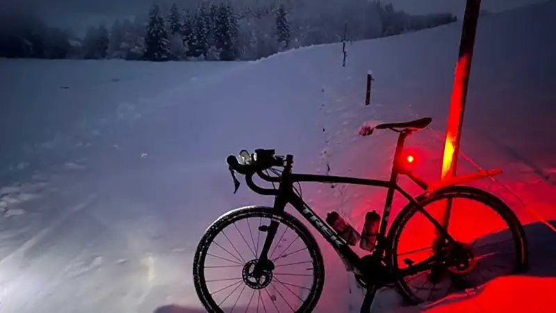 Ein Mountainbike auf verschneitem Feldweg, in der Dämmerung leuchtet das Rücklicht rot auf dem Schnee Ein Mountainbike auf verschneitem Feldweg, in der Dämmerung leuchtet das Rücklicht rot auf dem Schnee