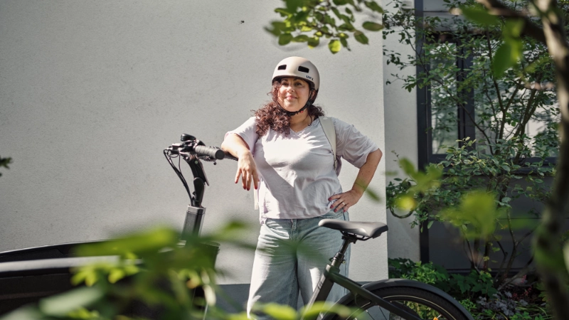Eine Frau lehnt stolz an ihrem Lastenrad und trägt einen Helm. Eine Frau lehnt stolz an ihrem Lastenrad und trägt einen Helm.