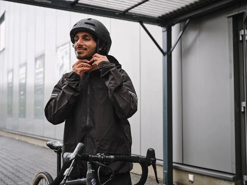Ein Mann mit Regenmantel zieht sich einen schwarzen Helm auf und steigt auf sein Fahrrad